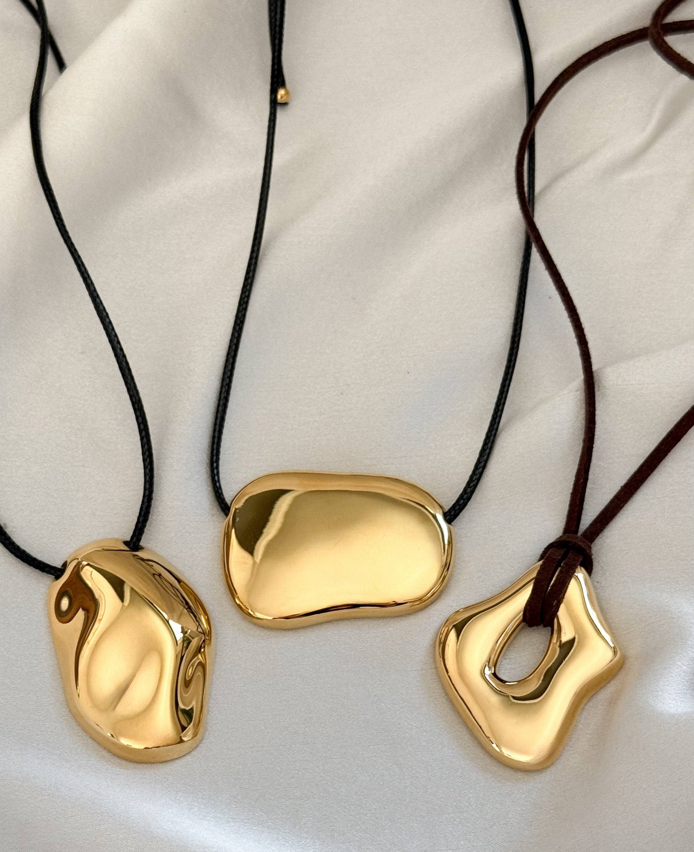 three gold moten statement necklaces with fabric strings and white background