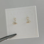 Pair of earrings on a clear card with 'THE SENSOR' branding, held by tweezers.