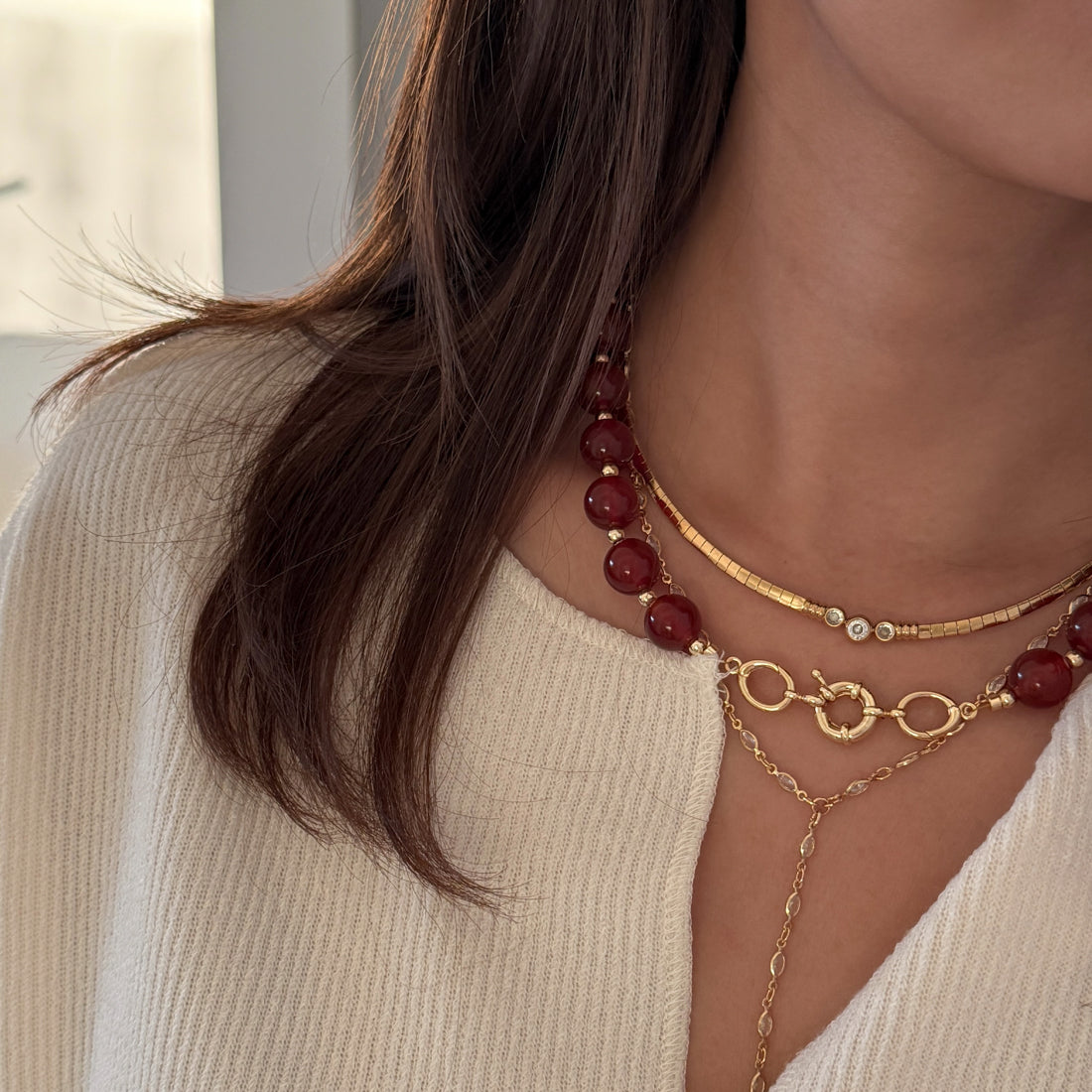 Close-up of a person wearing gold necklaces layered with red bead necklace.