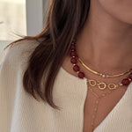 Close-up of a person wearing gold necklaces layered with red bead necklace.