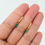 Gold earrings with green gemstones held between fingers on a white background