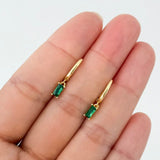 Gold earrings with green gemstones held between fingers on a white background