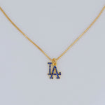 Gold necklace with a blue 'LA' pendant on a light gray background