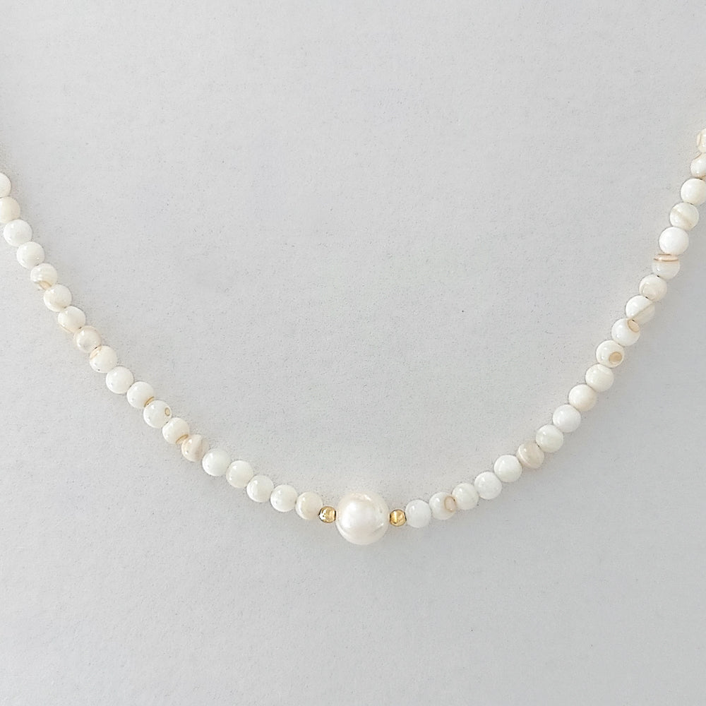 Pearl necklace with gold accents on a light gray background