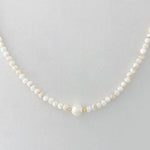 Pearl necklace with gold accents on a light gray background