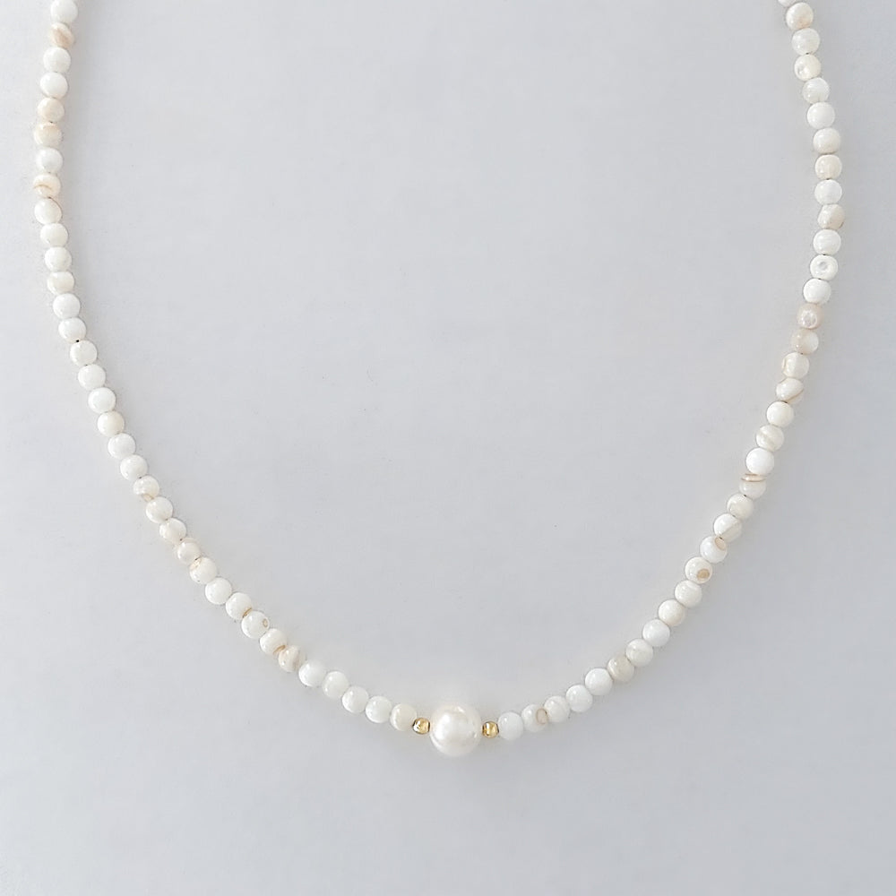 Pearl necklace with gold accents on a light gray background