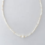 Pearl necklace with gold accents on a light gray background