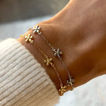Close-up of a wrist wearing a delicate gold bracelet with floral charms against a blurred background.