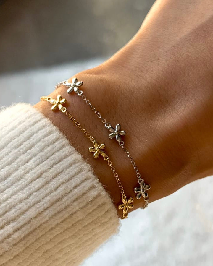 Close-up of a wrist wearing a delicate gold bracelet with floral charms against a blurred background.