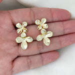 Gold flower-shaped earrings held in a hand on a white background