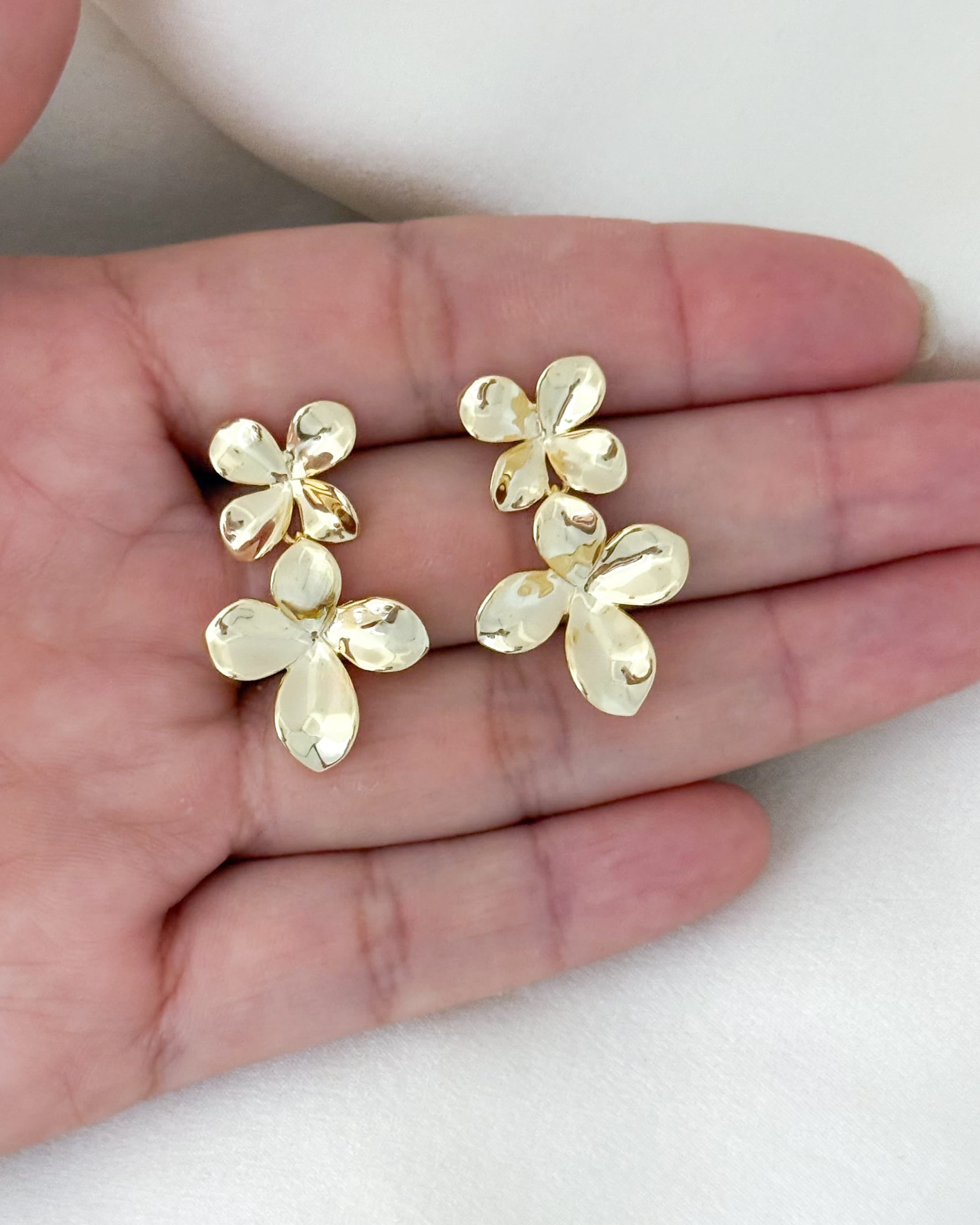 Gold flower-shaped earrings held in a hand on a white background