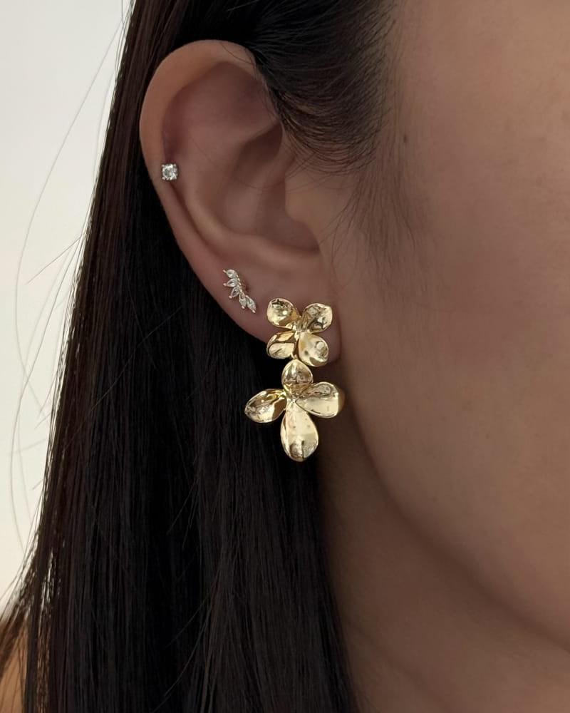Close-up of an ear wearing a gold floral earring with a blurred background