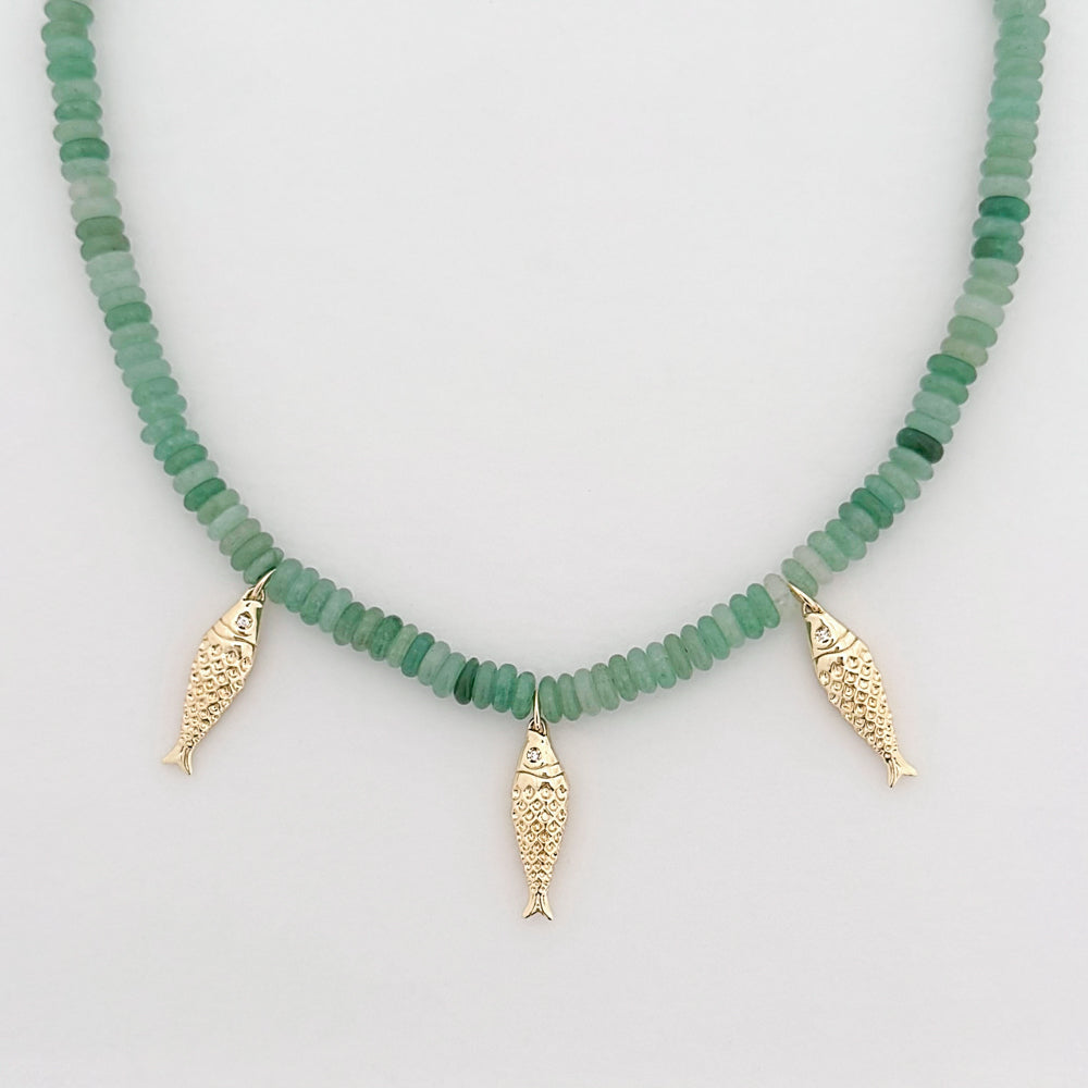 Necklace with green beads and three gold fish charms on a light gray background