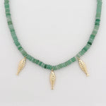 Necklace with green beads and three gold fish charms on a light gray background
