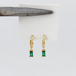Gold earrings with green gemstones on a white card
