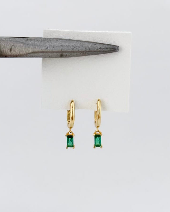 Gold earrings with green gemstones on a white card