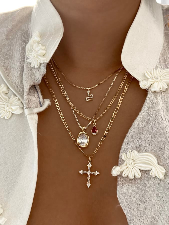 Layered gold necklaces with a cross pendant on a neutral background