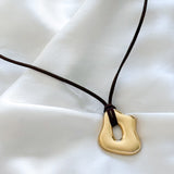 molten gold pendant on a dark brown suede cord against a white background