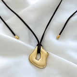 molten gold pendant necklace on a dark brown suede cord against a white fabric background