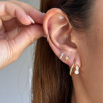 Close-up of a models ear wearing multiple small gold earrings, including a hoop, stud, and stacked bar earrings, with a hand adjusting the ear.