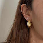 Close-up of an ear wearing gold twisted hoop earrings with a neutral background