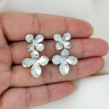 Silver floral earrings held in a hand against a white background