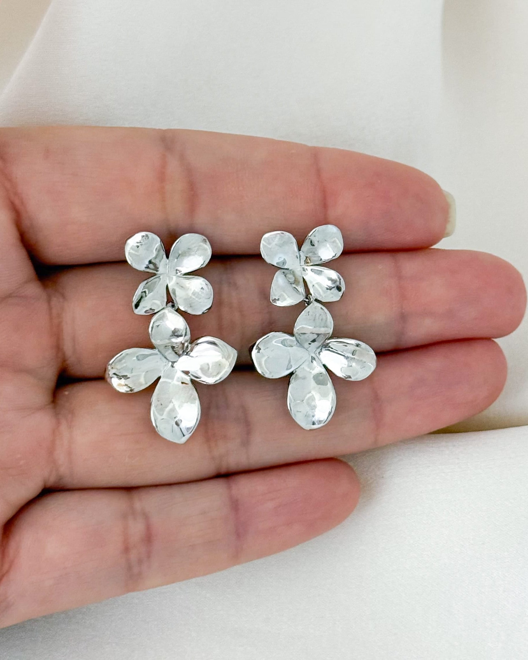 Silver floral earrings held in a hand against a white background