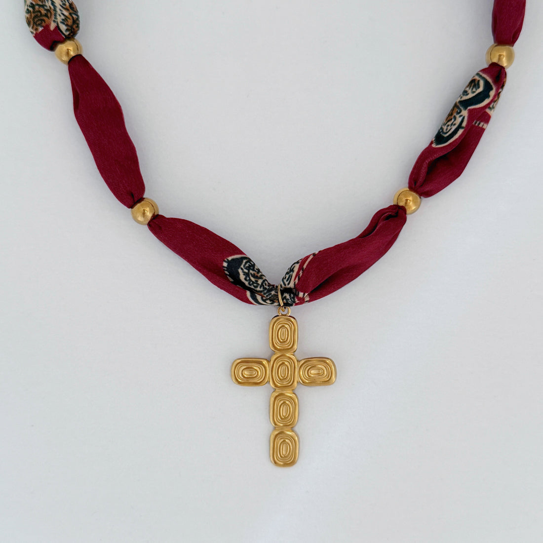 Statement necklace with stainless steel cross pendant and red patterned bandana wrap, displayed flat on a light gray background.
