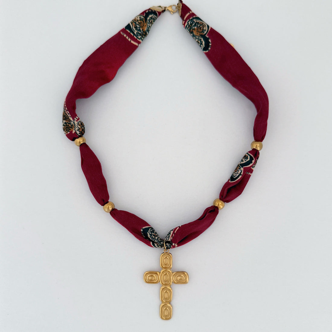 Red scarf fabric necklace with gold cross pendant on a white background