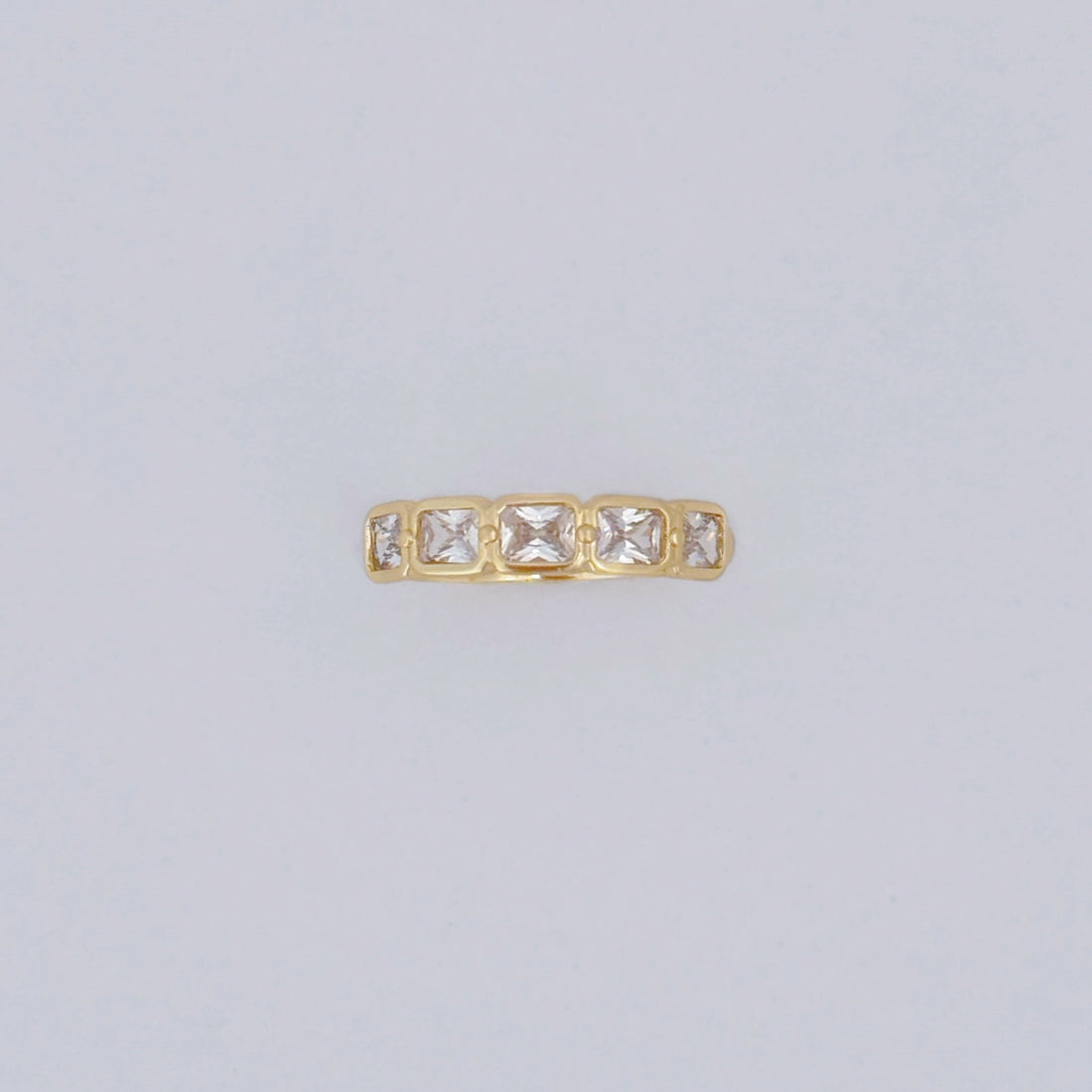 Gold ring with square-cut gemstones on a light gray background