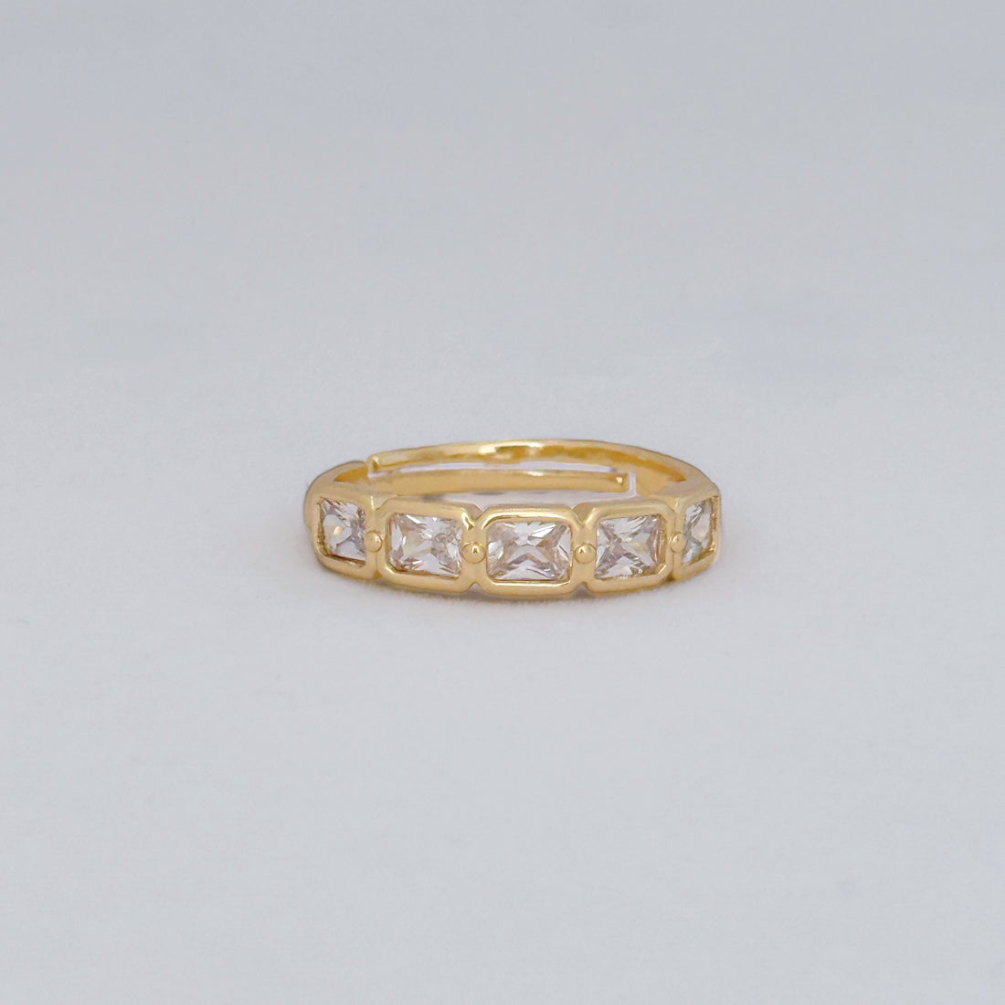 Gold ring with square-cut gemstones on a light gray background