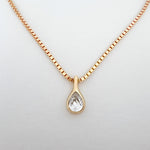 Gold necklace with a teardrop-shaped diamond pendant on a light gray background