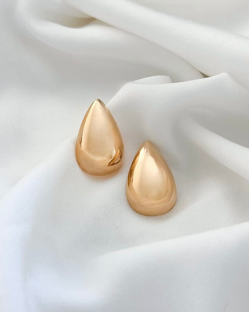Gold teardrop earrings on a white fabric background