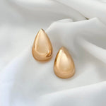 Gold teardrop earrings on a white fabric background