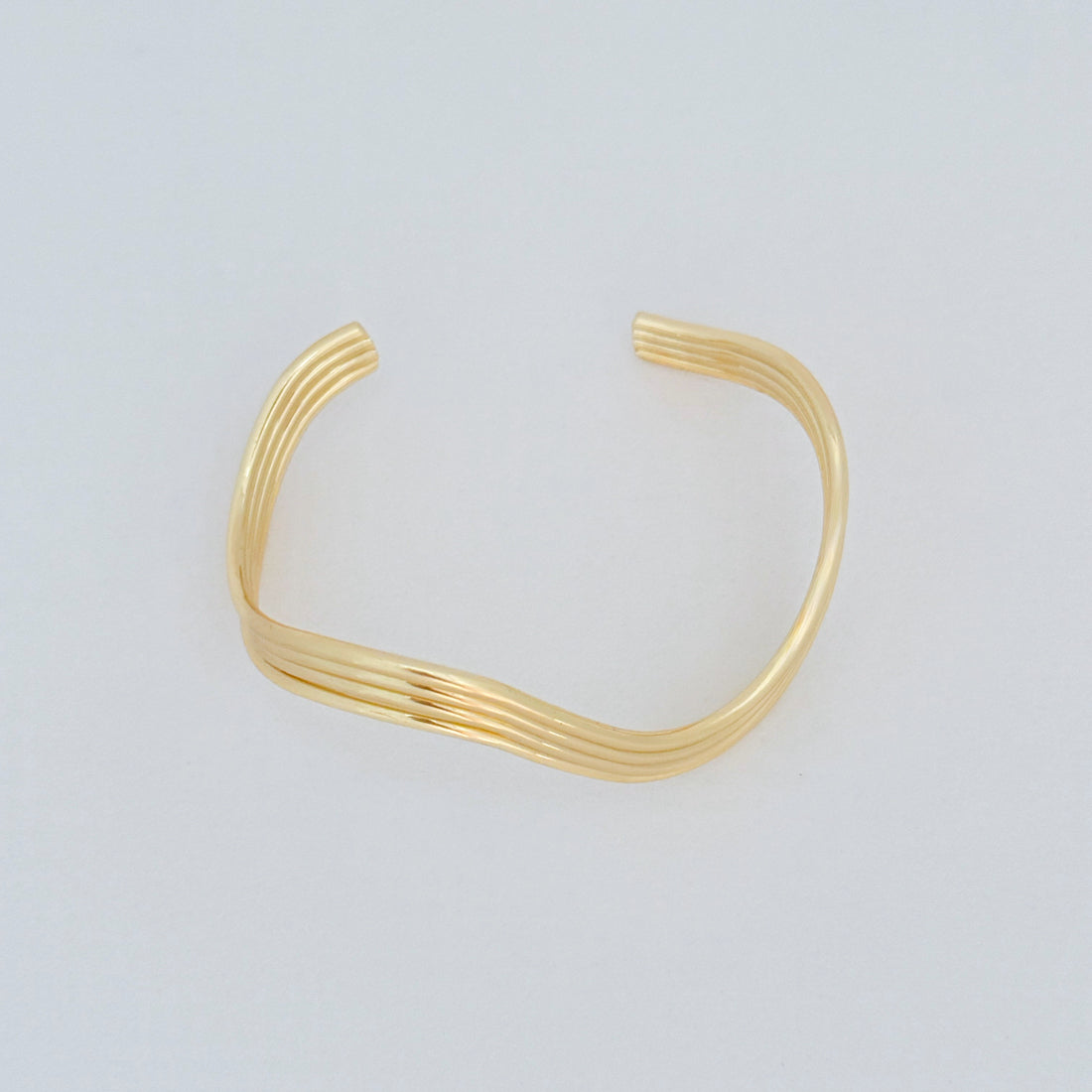 Minimalist wave-shaped gold-filled cuff bracelet displayed on grey background
