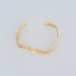 Minimalist wave-shaped gold-filled cuff bracelet displayed on grey background