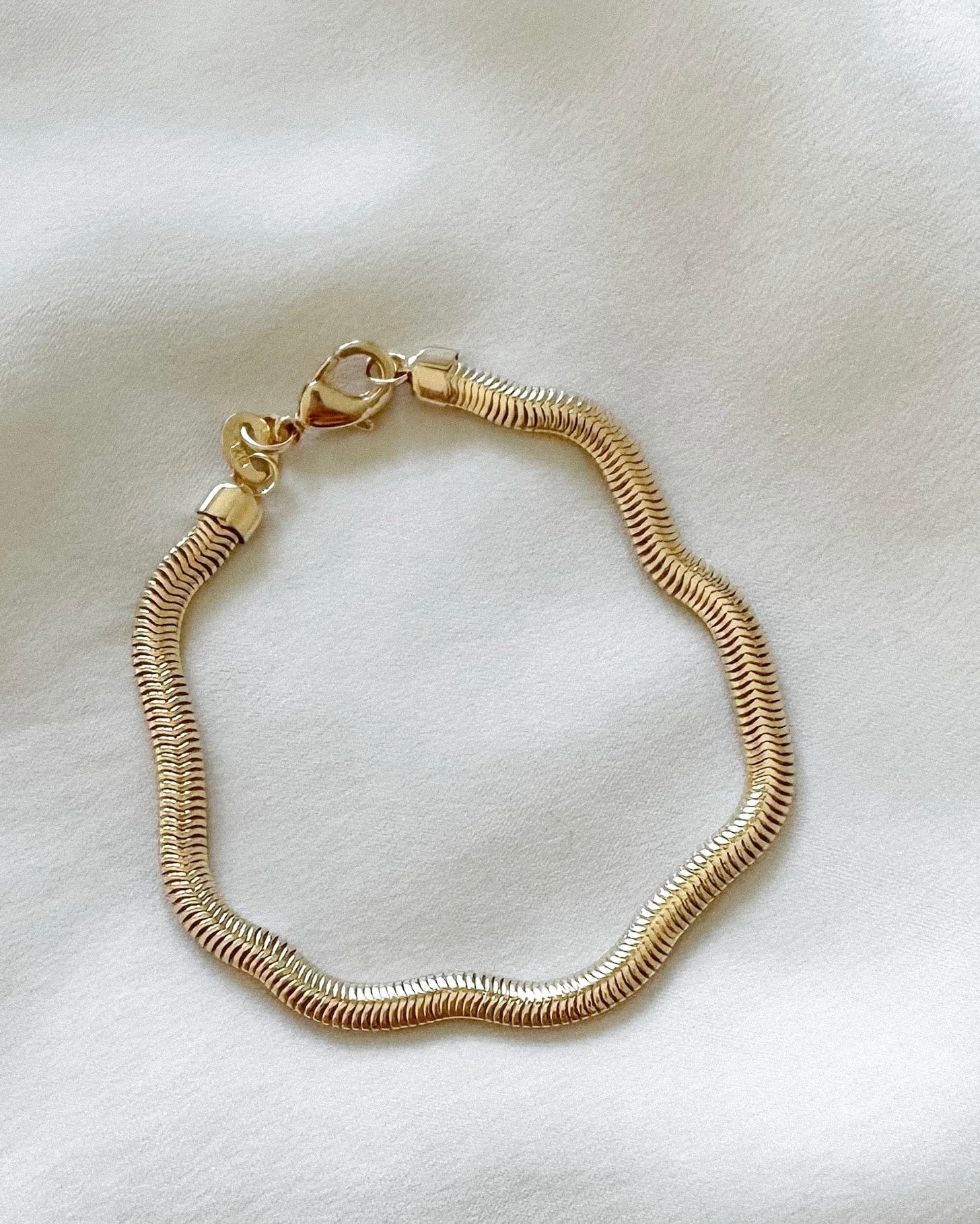 Gold flat snake chain bracelet on a light beige fabric background